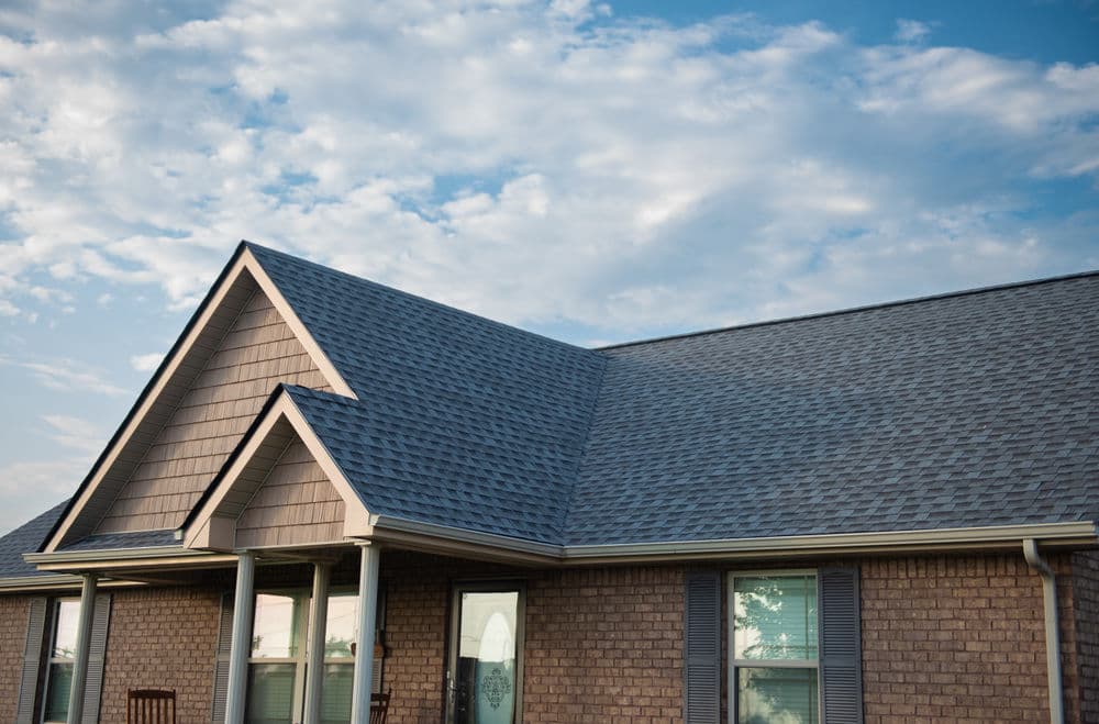 Brown brick house with a gable roof and cloudy blue sky in the background.